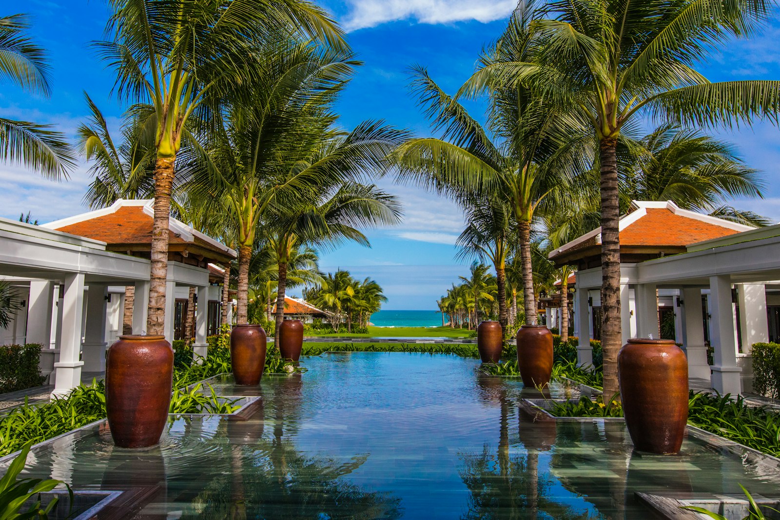 Luxury resort reflecting pool lined with symmetrical palms and villa pavilions opening to the sea at Hoi An